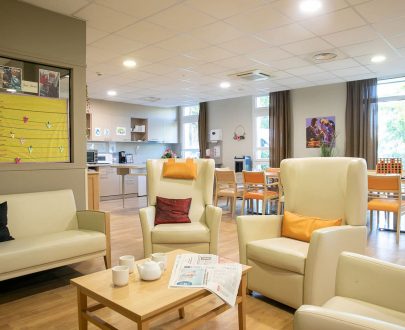 Espace d'accueil de jour avec espace salon, tables d'activité, petite cuisine et bureau vitré de la maîtresse de maison